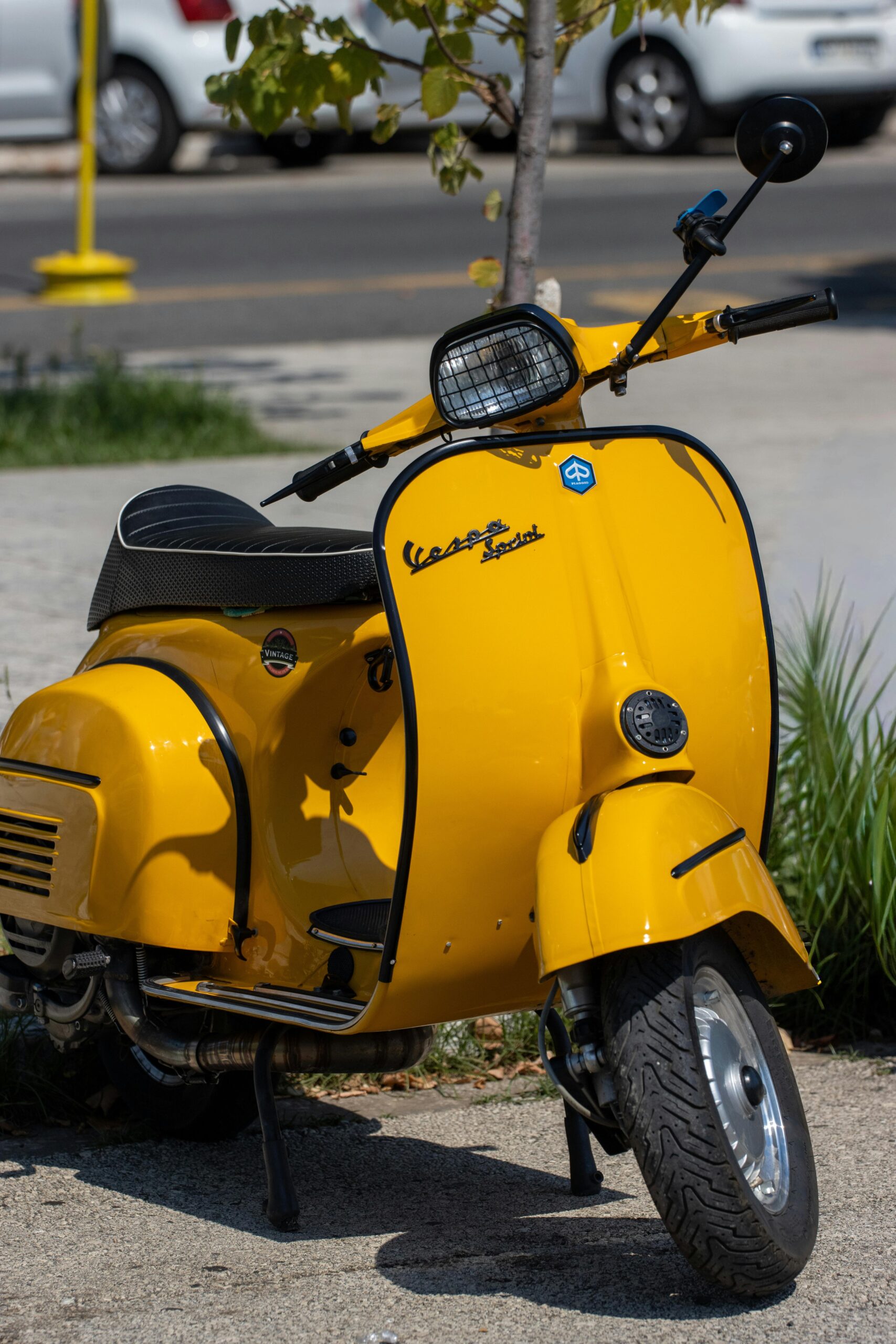 A classic yellow Vespa stands out on a sunny street in Corfu, Greece, against a backdrop of greenery.